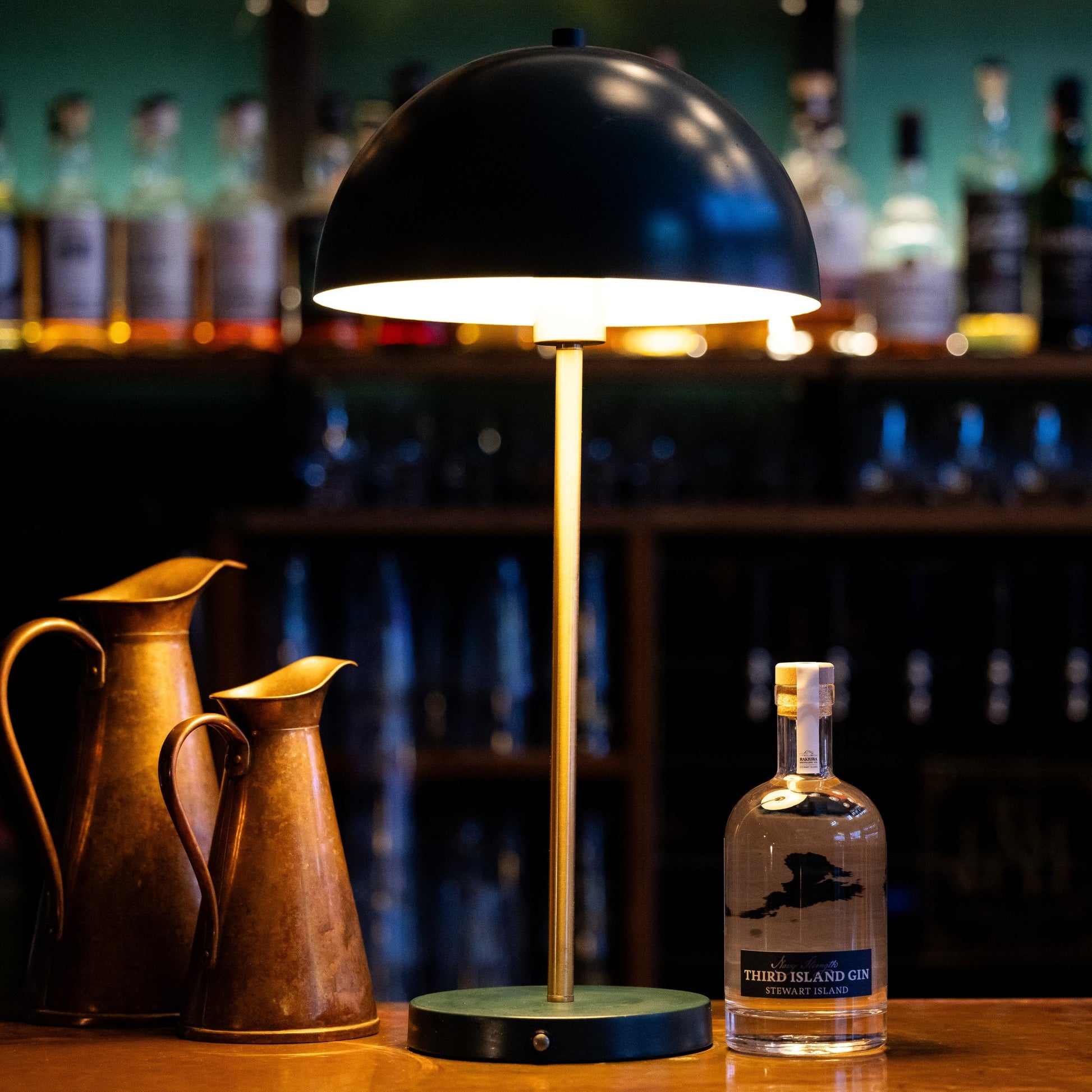 Table lamp and bottle of Third Island Navy Strength Gin on a bar counter with blurred bottles in the background