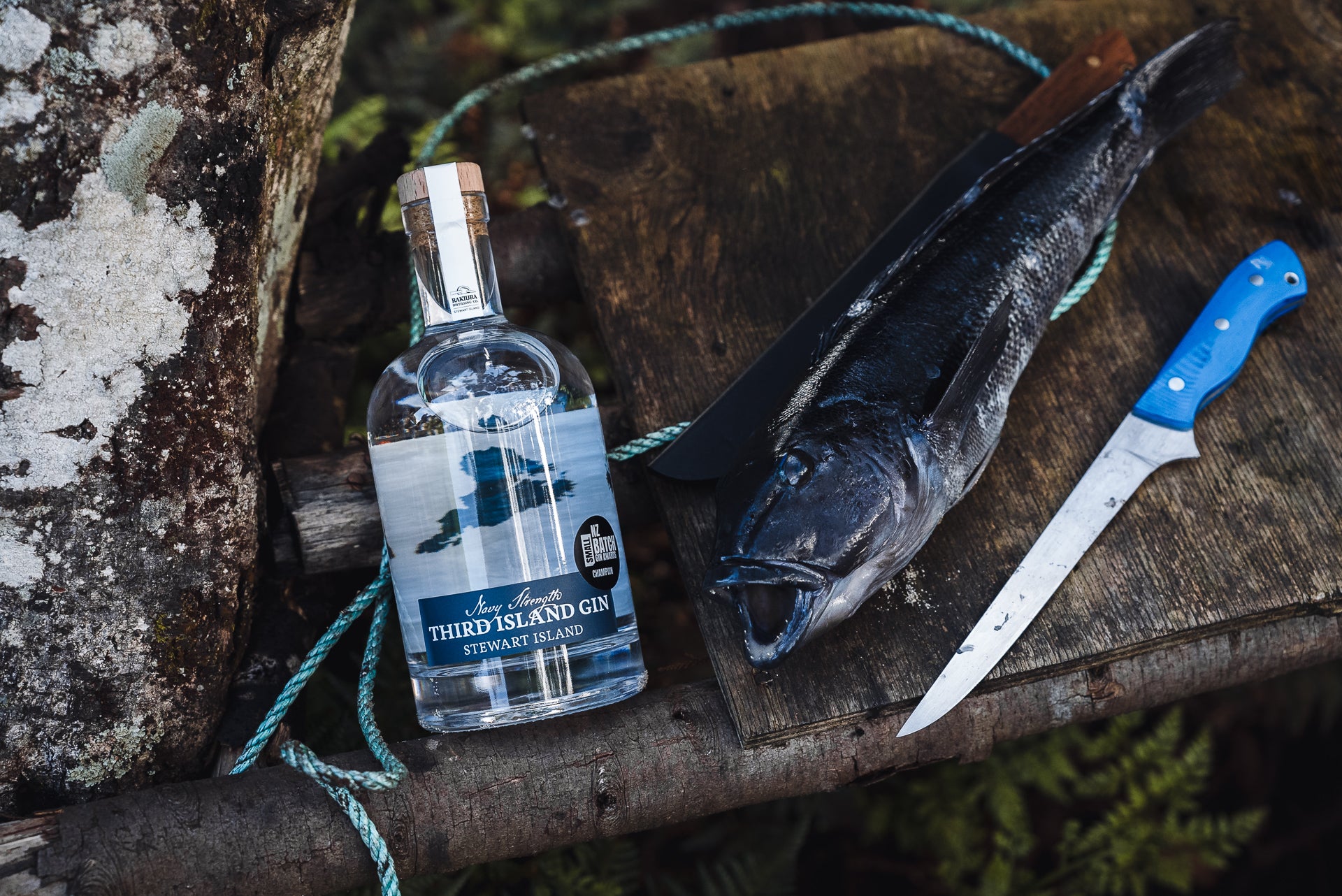 Bottle of Third Island Navy Strength Gin on a wooden surface with a fish and knife.