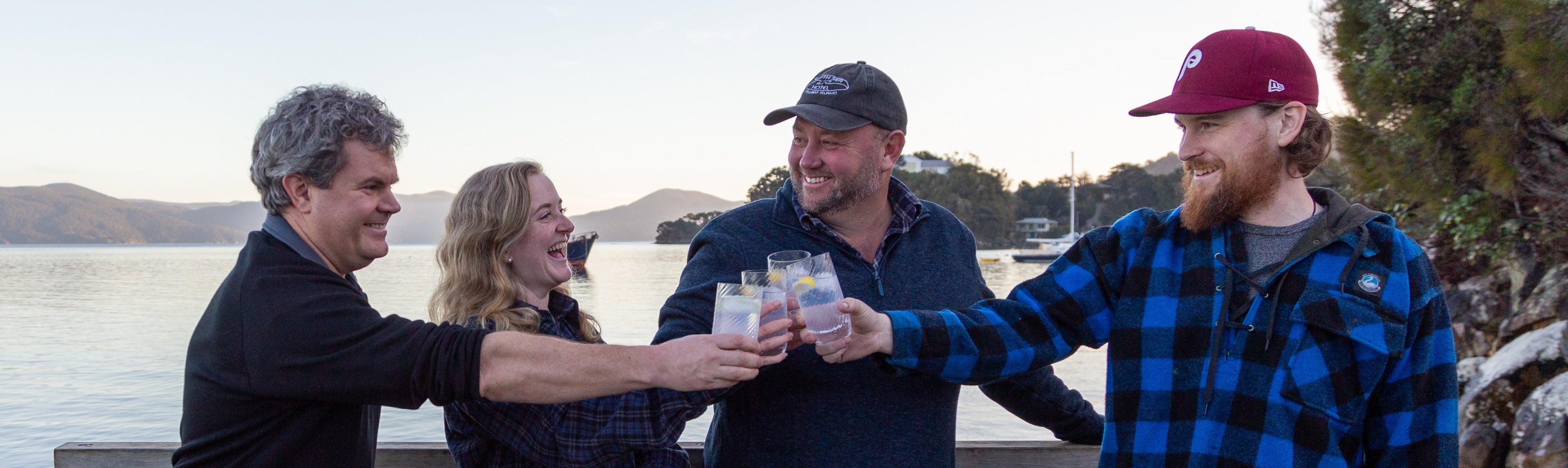 Four people toasting with glasses by a body of water