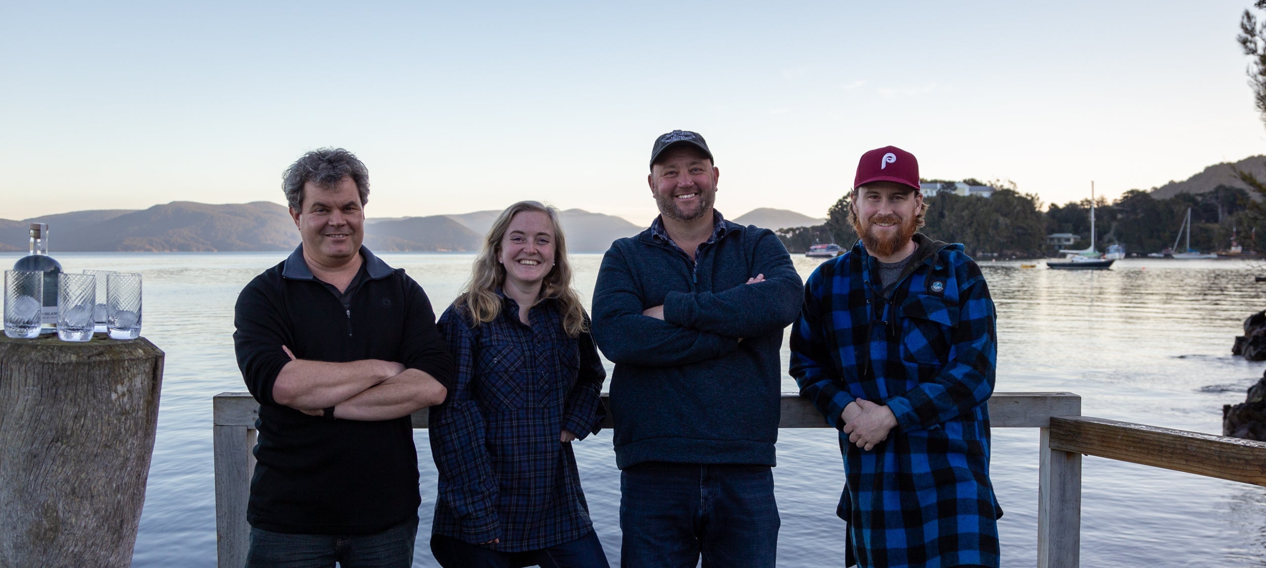 Four people standing on a dock by a body of water with mountains in the background.